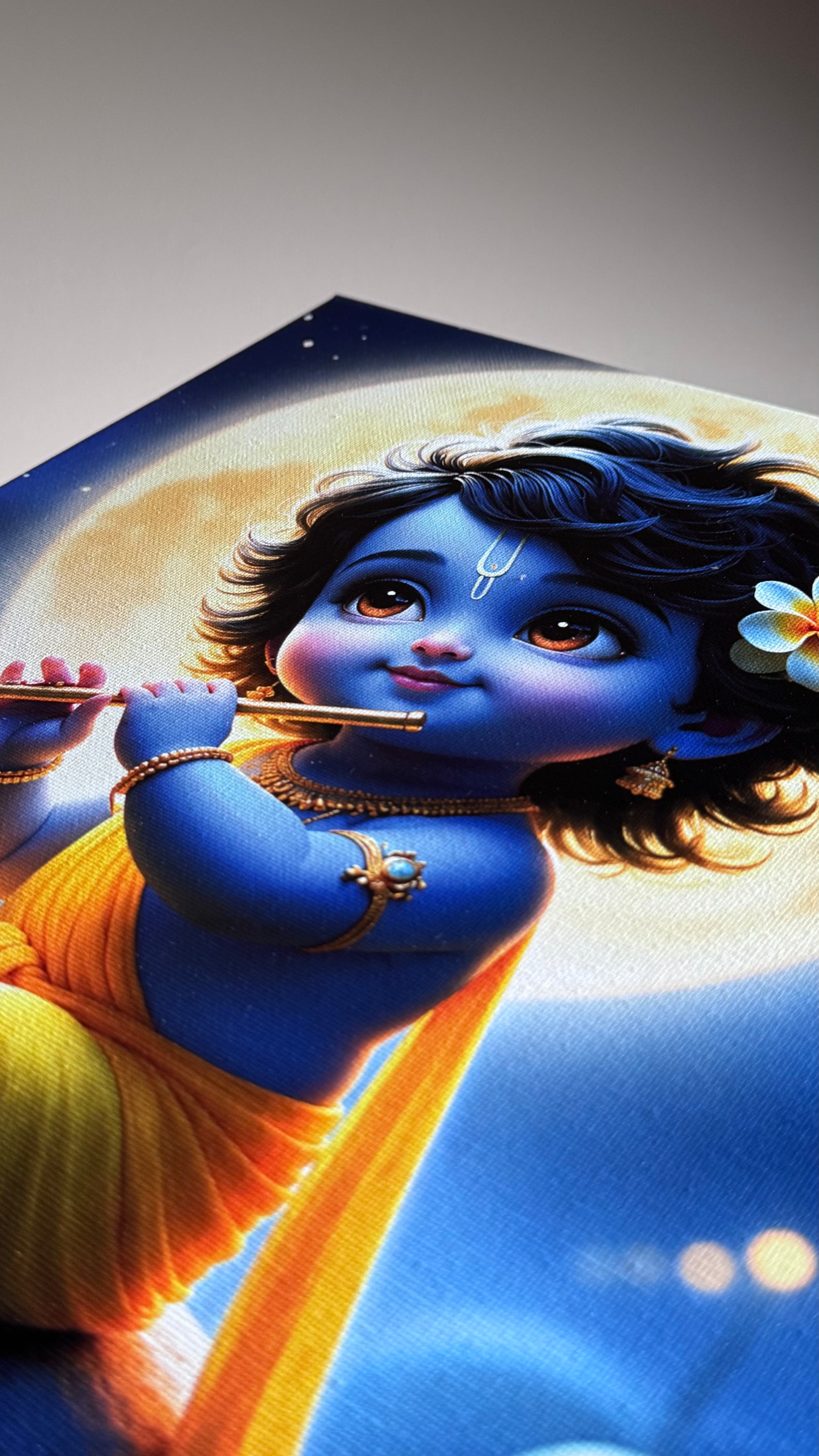 A close-up of a printed artwork or poster showing a blue-skinned child playing a flute, with a yellow drape, dark hair, and a flower, set against a blue and cream background.