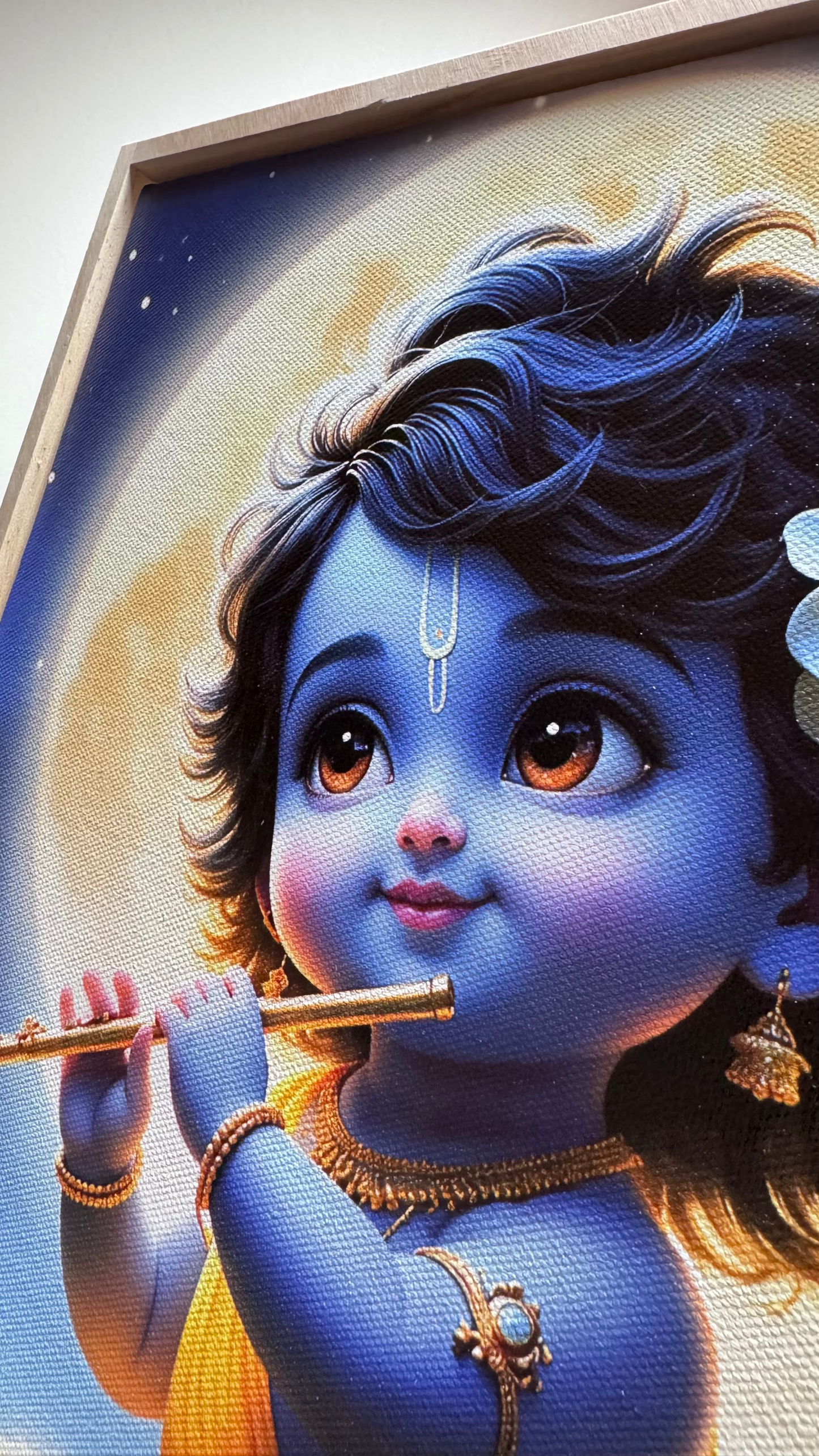 A close-up of a framed artwork depicting a blue-skinned child with large brown eyes holding a flute, with warm golden light in the background and a visible frame edge.