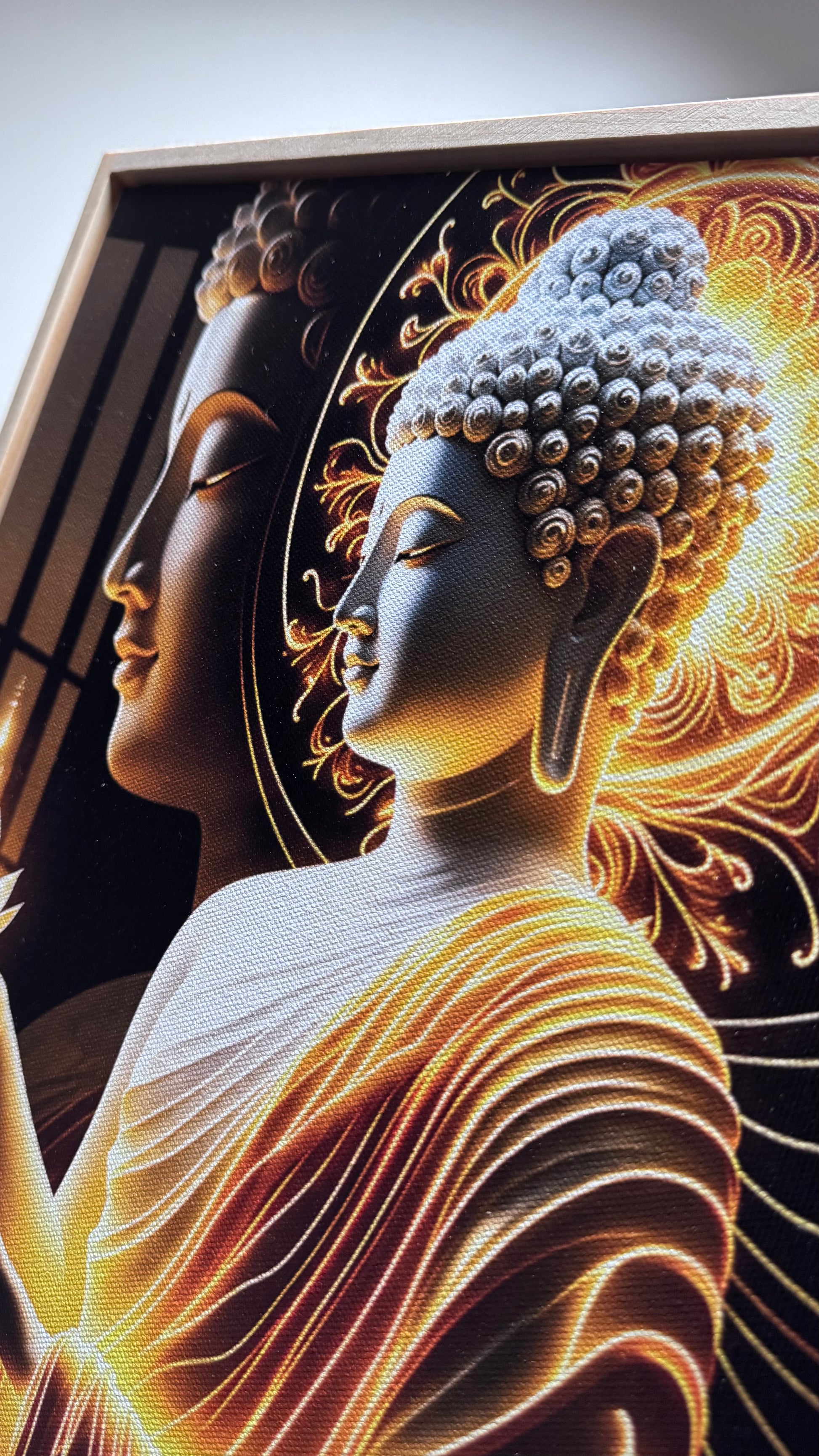 A close-up of a framed artwork featuring a stylized Buddha head and shoulders in profile, rendered in glowing gold, orange, and cream tones against a dark background.
